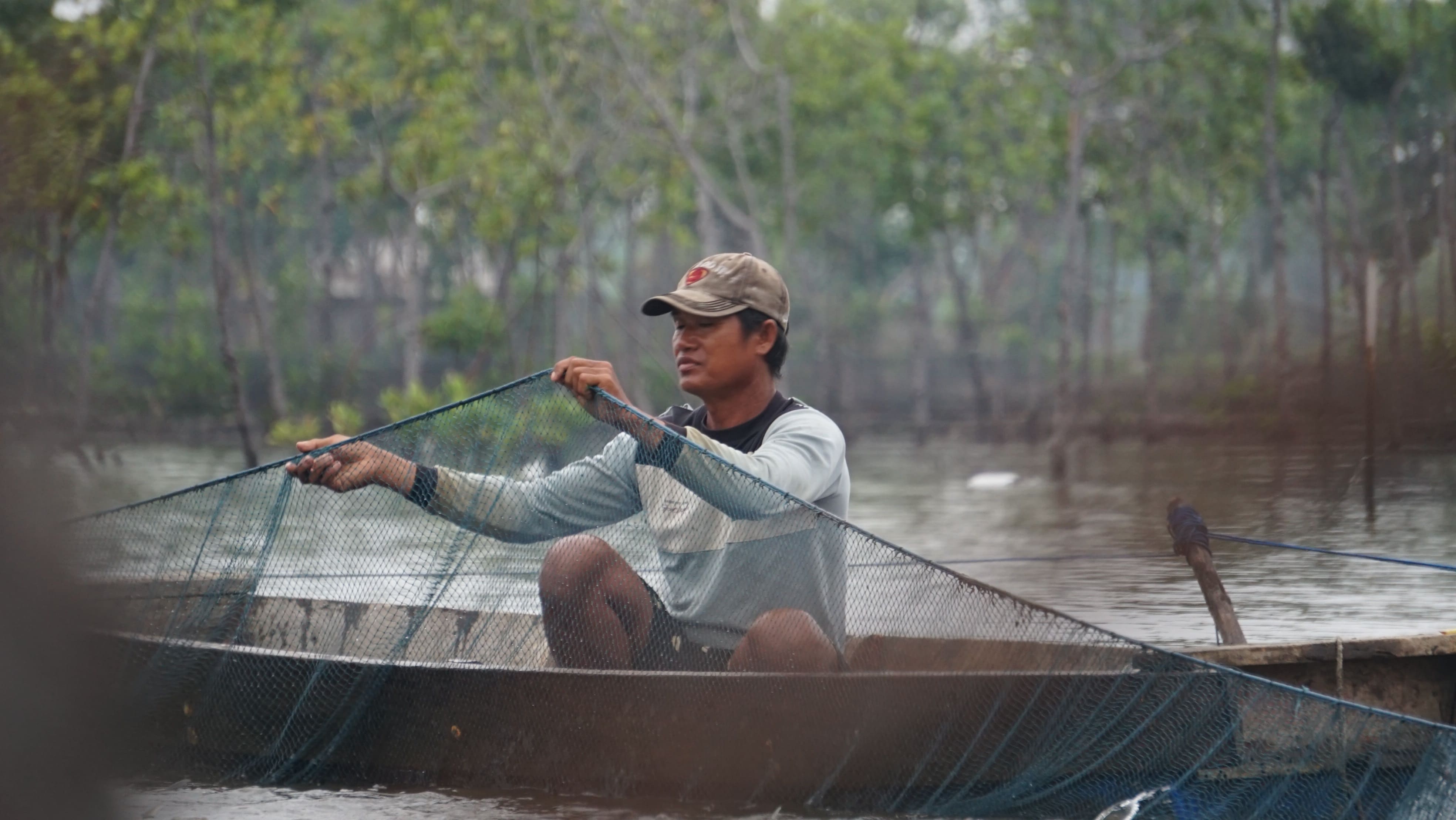Seorang pembudidaya ikan bandeng di daerah pesisir yang sedang melakukan kegiatan panen menggunakan jaring diatas perahu